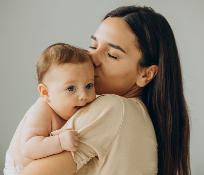 Woman carrying her baby, kissing her on the forehead